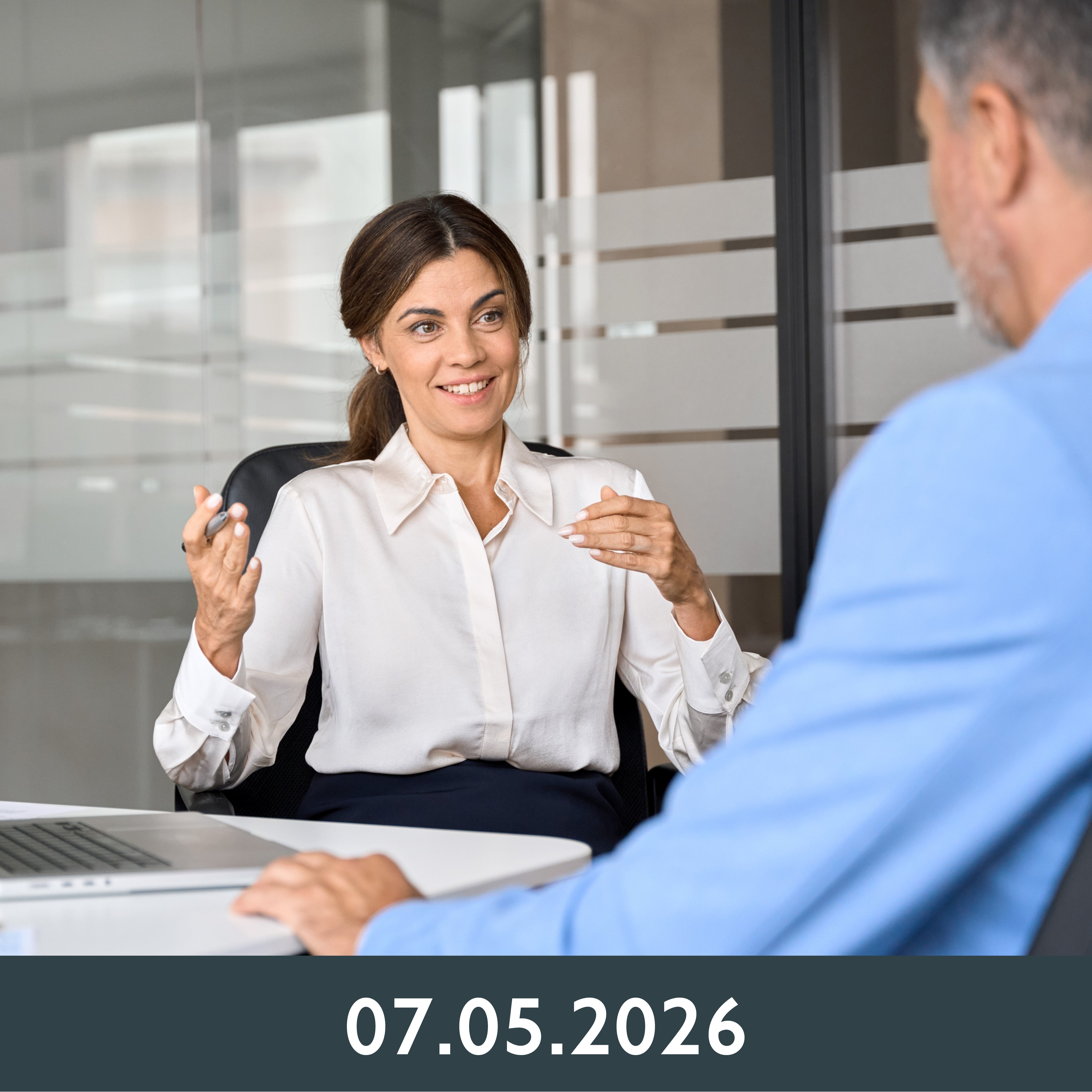 Eine Frau unterhält sich freundlich mit einem Mann in einem blauen Hemd. Sie sitzen an einem modernen Bürotisch und vermitteln eine Atmosphäre der Zusammenarbeit auf Augenhöhe.