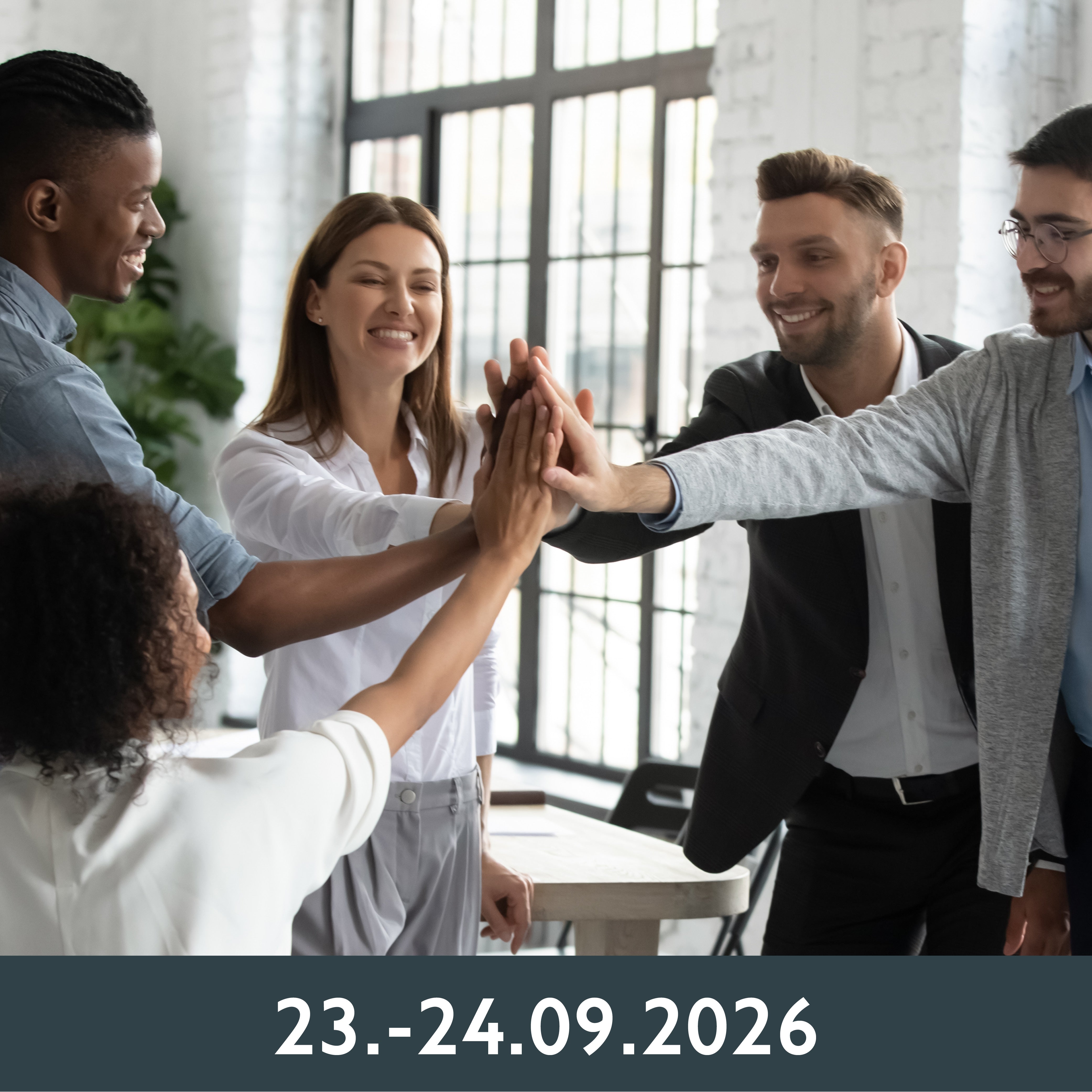 Eine Gruppe von fünf Kollegen steht in einem Büro und klatscht sich freudig ab. Große Fenster und eine helle Atmosphäre suggerieren Teamwork und Erfolg.